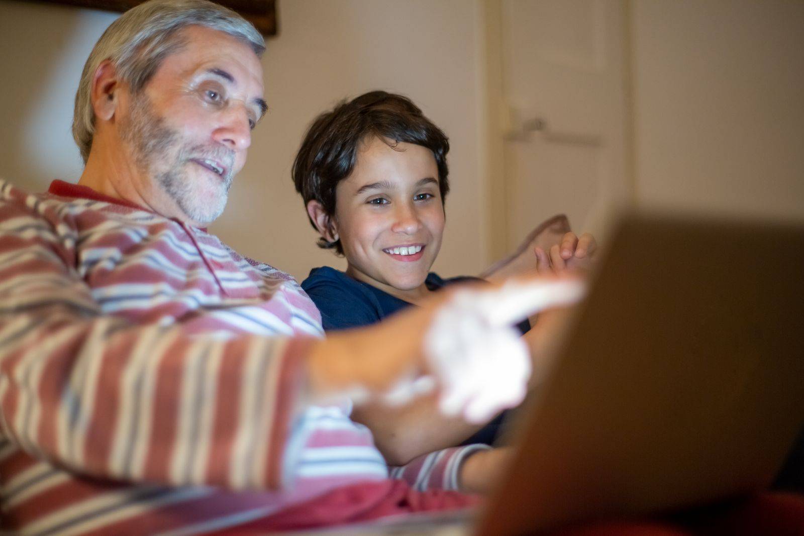 Un grand-père et un jeune garçon souriants devant un ordinateur portable.